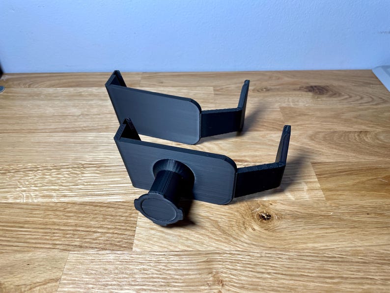 May include: Two black plastic camera mounts with a threaded hole for a tripod. The mounts are designed to be attached to a surface.
