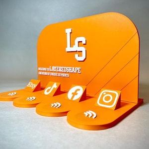 May include: An orange display stand with white text and social media icons. The stand features the Etsy, TikTok, Facebook, and Instagram logos. The text on the stand reads "LS" and "WELCOME TO LAYEREDSHAPE CREATORS OF UNIQUE 3D PRINTS."