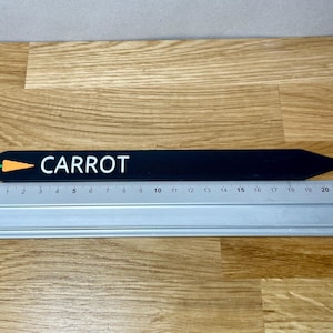 May include: Black wooden plant marker with a white "CARROT" label and a small orange carrot graphic. The marker is 20 cm long.