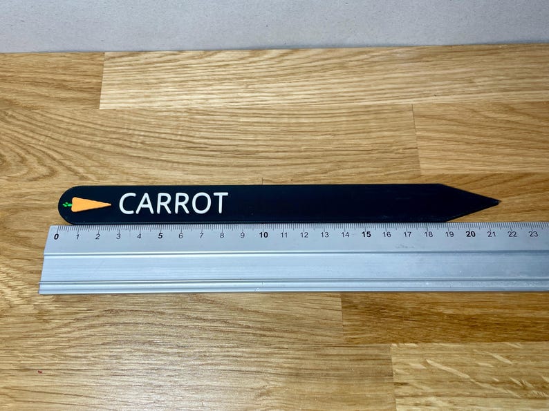 May include: Black wooden plant marker with a white "CARROT" label and a small orange carrot graphic. The marker is 20 cm long.
