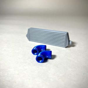May include: A gray intercooler with horizontal fins and two bright blue, curved pipe fittings. The components are likely for an automotive or mechanical application, set against a neutral background.