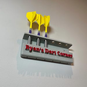 Wall mounted dart holder. Grey with red personalised text on the front reading Ryan's Dart Corner