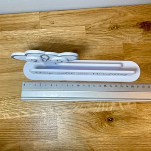 May include: White wooden sign with the text "Days until our wedding" and a number display. The sign is sitting on a wooden surface with a ruler next to it.