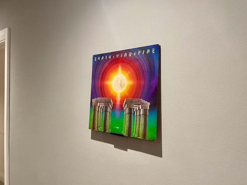 May include: A vintage vinyl record album cover featuring a colorful illustration of a sun with rays of light shining down on a row of columns. The album cover is titled "Earth, Wind & Fire" in a stylized font.