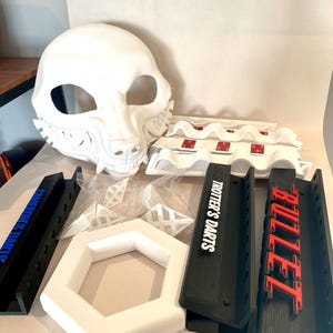 May include: A collection of white and black 3D-printed items. Includes a white animal mask, black dart holders with "TROTTER'S DARTS" and "BULLET" text, and a white hexagonal frame. Also, there are some white plastic pieces.