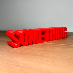 Pu&ograve; includere: Un cartello rosso brillante, stampato in 3D, con la scritta "SOMETHING". Le lettere a blocchi sono su una superficie di legno. Un elemento decorativo accattivante.
