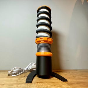 Op de afbeelding: Een zwarte en oranje desktopmicrofoon met een veerachtig ontwerp en een basis met een gebogen vorm.