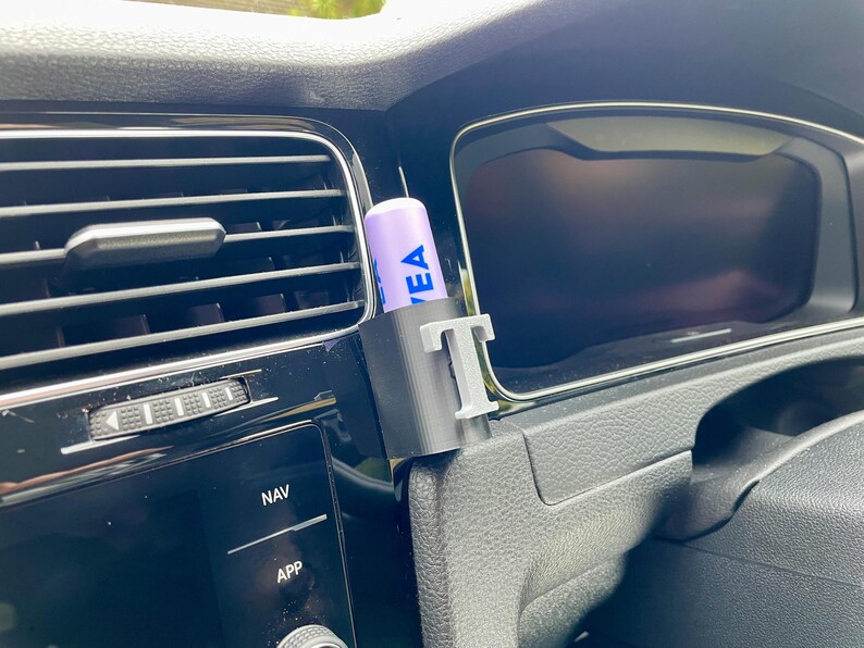 Pu&ograve; includere: Un supporto per telefono da auto stampato in 3D di colore grigio con la lettera "T" stampata su di esso. Un balsamo per labbra viola con la parola "EA" stampata su di esso &egrave; nel supporto. Il supporto &egrave; attaccato alla ventola di un'auto.
