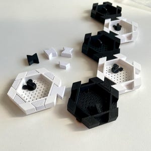 May include: A collection of black and white hexagonal trays with a perforated interior and a Mickey Mouse head design. Several small black and white geometric shapes are scattered nearby. The trays are arranged in a line.