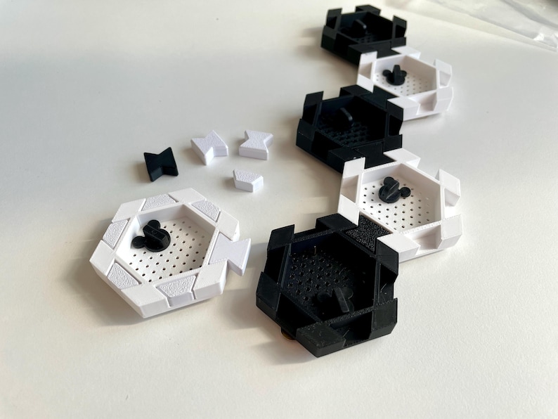 May include: A collection of black and white hexagonal trays with a perforated interior and a Mickey Mouse head design. Several small black and white geometric shapes are scattered nearby. The trays are arranged in a line.