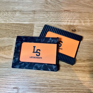 May include: Two black card holders with orange inserts. The top card holder has a carbon fiber pattern and the text "SHAPE" on the insert. The bottom card holder has a geometric pattern and the text "LS LAYEREDSHAPE" on the insert.