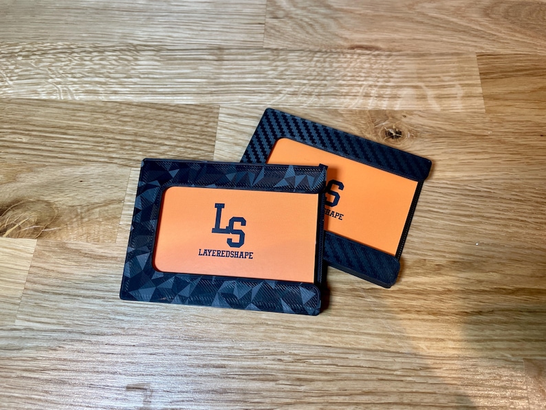 May include: Two black card holders with orange inserts. The top card holder has a carbon fiber pattern and the text "SHAPE" on the insert. The bottom card holder has a geometric pattern and the text "LS LAYEREDSHAPE" on the insert.
