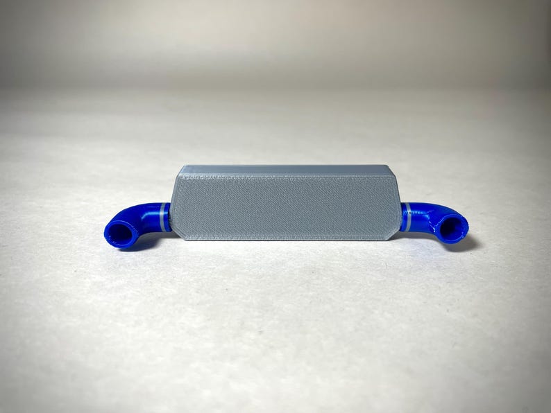 May include: A small, rectangular, gray object with blue, curved tubes extending from each end. The gray body has a textured surface. The blue tubes have a white stripe. The object is likely a component or part of a larger system.