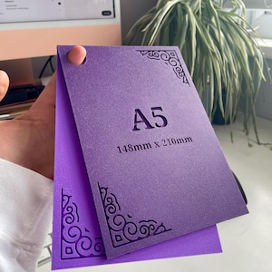 May include: A purple A5 card measuring 148mm x 210mm with a textured surface. The card features intricate, dark purple decorative corner patterns and a circular hole punch in the top left corner. The text A5 and 148mm x 210mm is printed.