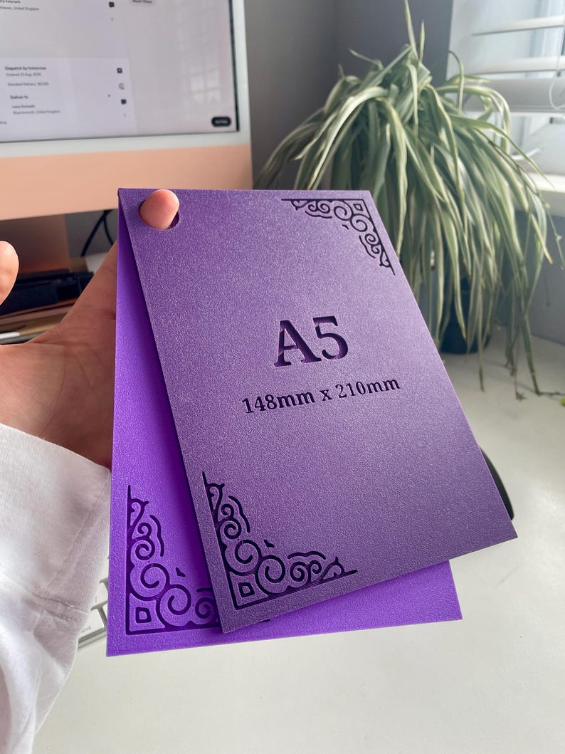 May include: A purple A5 card measuring 148mm x 210mm with a textured surface. The card features intricate, dark purple decorative corner patterns and a circular hole punch in the top left corner. The text A5 and 148mm x 210mm is printed.