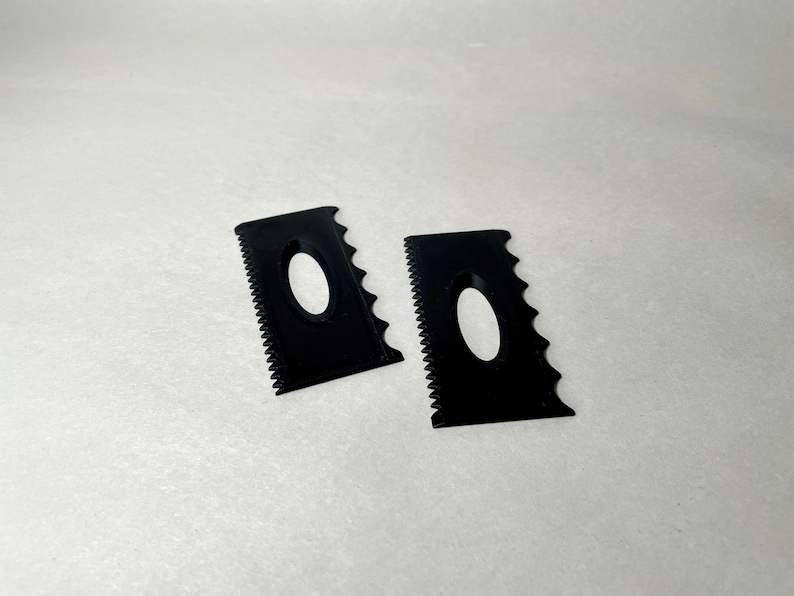 May include: Two black pottery rib tools with a serrated edge and an oval cutout. These tools are used for shaping and smoothing clay in pottery and ceramics.