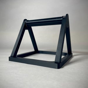 May include: A black push-up bar with a rectangular base and angled supports. The bar is cylindrical and connects the two angled supports. The design is minimalist and modern, suitable for home fitness.
