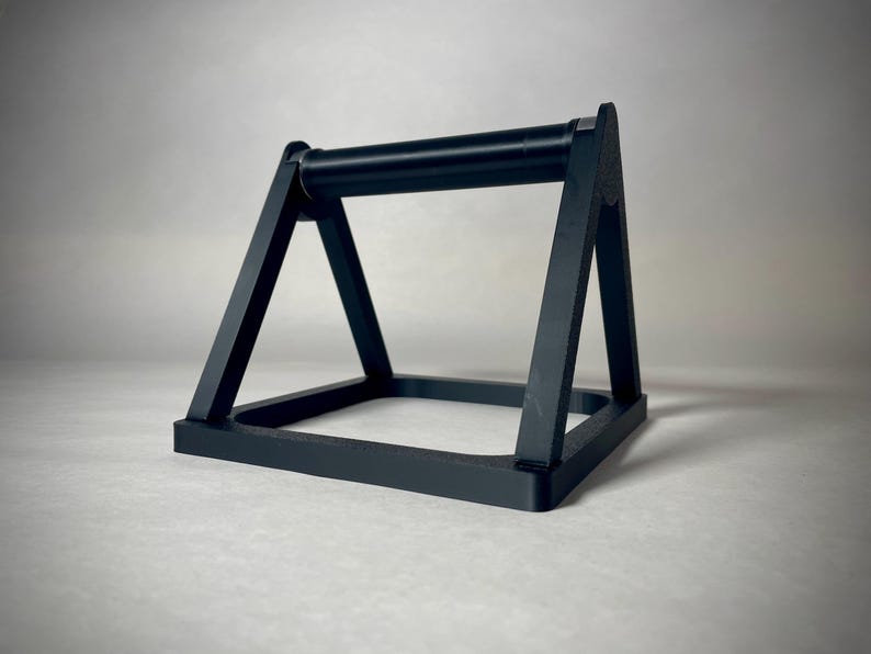 May include: A black push-up bar with a rectangular base and angled supports. The bar is cylindrical and connects the two angled supports. The design is minimalist and modern, suitable for home fitness.