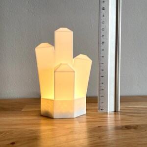Pu&ograve; includere: Una lampada bianca a forma di cristallo con una luce calda e brillante. La lampada &egrave; realizzata in un materiale bianco liscio e ha un design geometrico.