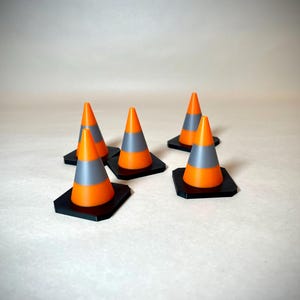May include: A group of small orange and grey traffic cones with black square bases. The cones are set against a neutral backdrop, highlighting their bright colours and design.
