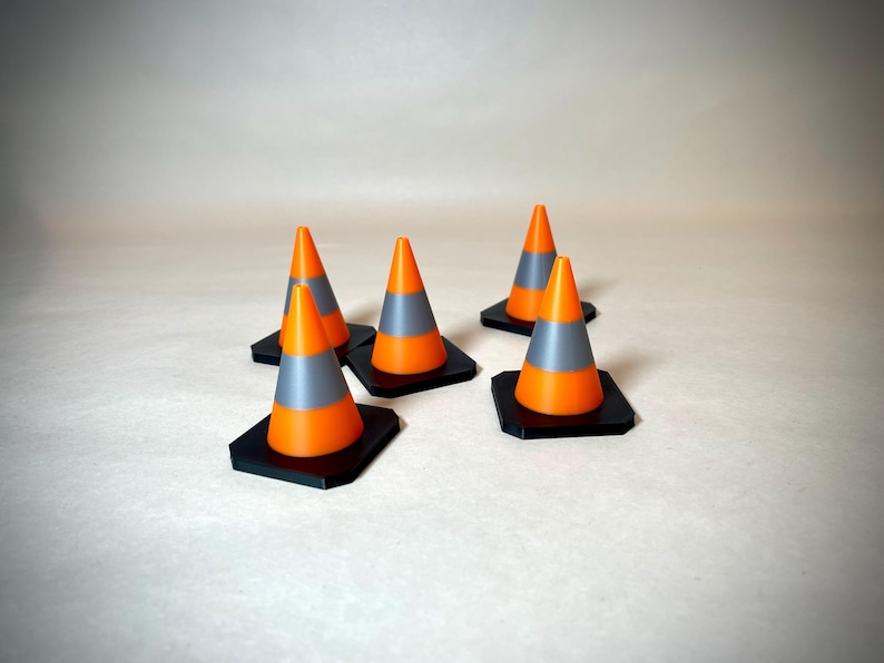 May include: A group of small orange and grey traffic cones with black square bases. The cones are set against a neutral backdrop, highlighting their bright colours and design.