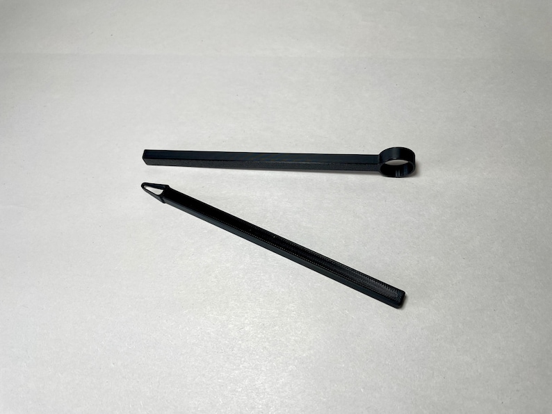 May include: Two black tools are displayed against a white background. One tool is a long, thin rod with a circular end. The other is a similar rod with a pointed tip. Both tools appear to be made of plastic.
