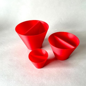 May include: Three bright red, cone-shaped objects with a central divider. The objects vary in size, with the smallest being a miniature version of the larger two. The objects are set against a plain, off-white background.