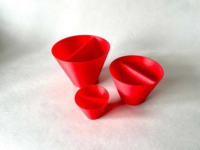 May include: Three bright red, cone-shaped objects with a central divider. The objects vary in size, with the smallest being a miniature version of the larger two. The objects are set against a plain, off-white background.