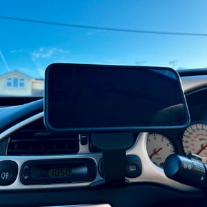 May include: A black phone mount attached to the dashboard of a car. The phone mount is holding a black smartphone. The car's dashboard has a digital clock that reads 10:50.