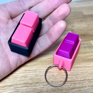 May include: Two keychains with a pink and purple square design. The keychains are made of plastic and have a metal ring.