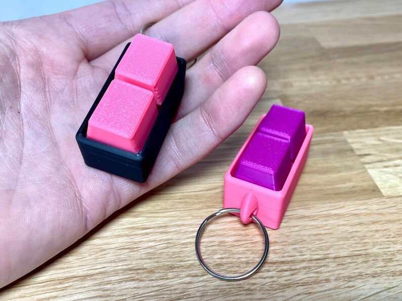 May include: Two keychains with a pink and purple square design. The keychains are made of plastic and have a metal ring.
