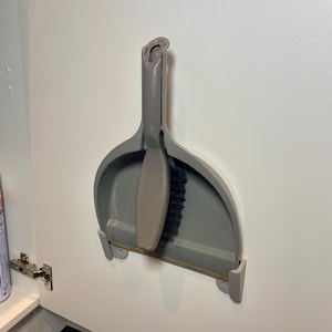 grey dust pan hung on the inside of a kitchen cabinet door