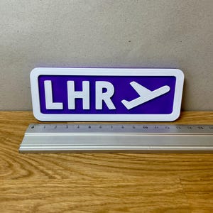 May include: A purple and white sign with the text "LHR" and a white airplane icon.