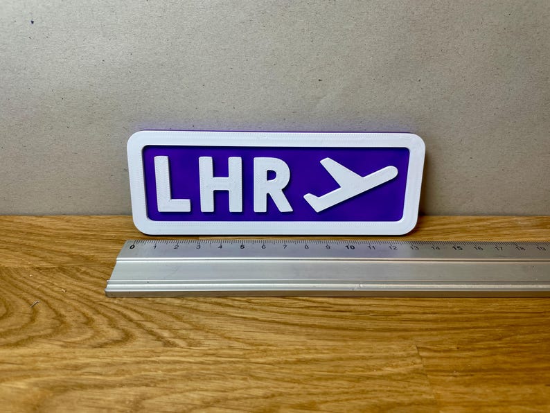 May include: A purple and white sign with the text "LHR" and a white airplane icon.