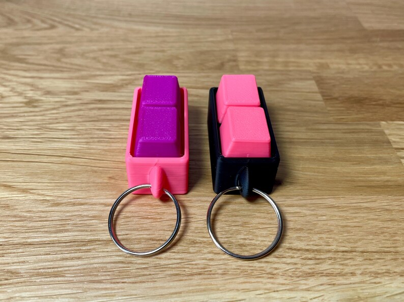 May include: Two keychains with pink and purple keycaps attached to silver key rings. The keychains are made of black and pink plastic.