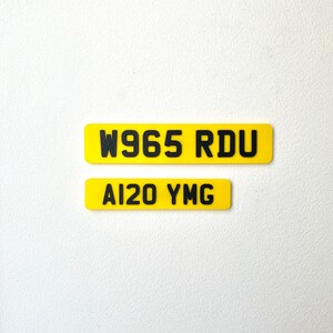 May include: Two yellow rectangular license plates with black text. The top plate reads "W965 RDU" and the bottom plate reads "AI20 YMG". The plates are set against a white background.