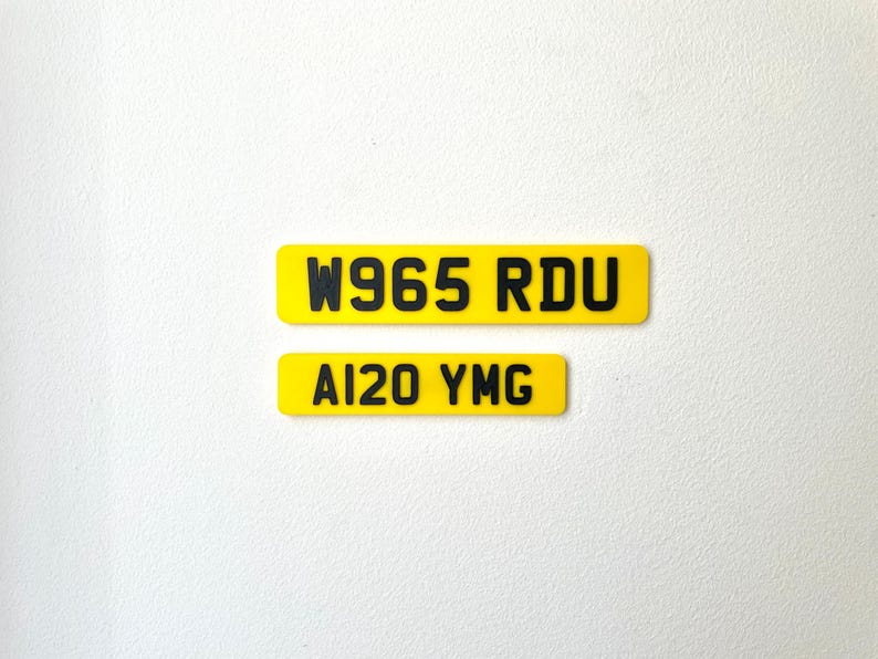 May include: Two yellow rectangular license plates with black text. The top plate reads "W965 RDU" and the bottom plate reads "AI20 YMG". The plates are set against a white background.