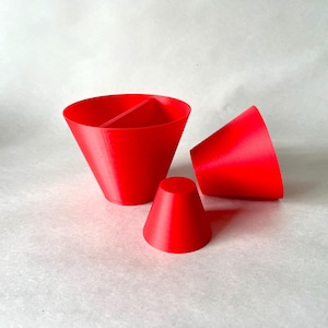 May include: Three bright red, cone-shaped objects are arranged on a light background. One is a large, divided cone, another is a smaller cone, and the third is a cone lying on its side. The objects appear to be 3D printed.