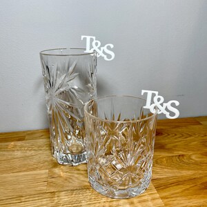 Tumbler and tall glass with a set of initial letters clipped onto the side. Drink topper is white and the photo shows a grey background.
