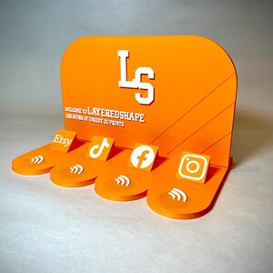 May include: Orange display stand with white text and social media icons for Etsy, TikTok, Facebook, and Instagram. The stand features the text "WELCOME TO LAYEREDSHAPE CREATORS OF UNIQUE 3D PRINTS" and the initials "LS".