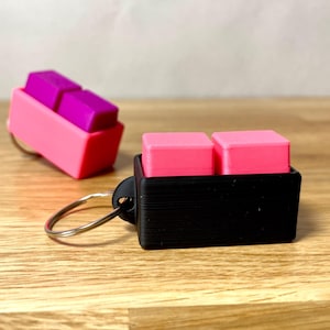 May include: A black keychain with a pink and purple keycap holder. The keychain has a silver ring.