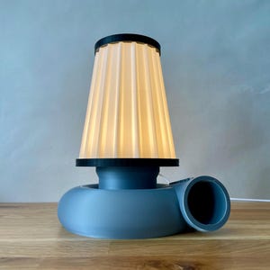 Puede incluir: Una l&aacute;mpara de mesa azul y blanca con una pantalla de tela plisada. La base de la l&aacute;mpara tiene forma de turbina.