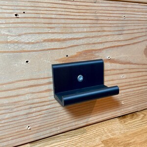 May include: A black plastic wall mount with a small shelf. The shelf is attached to the wall with a screw.