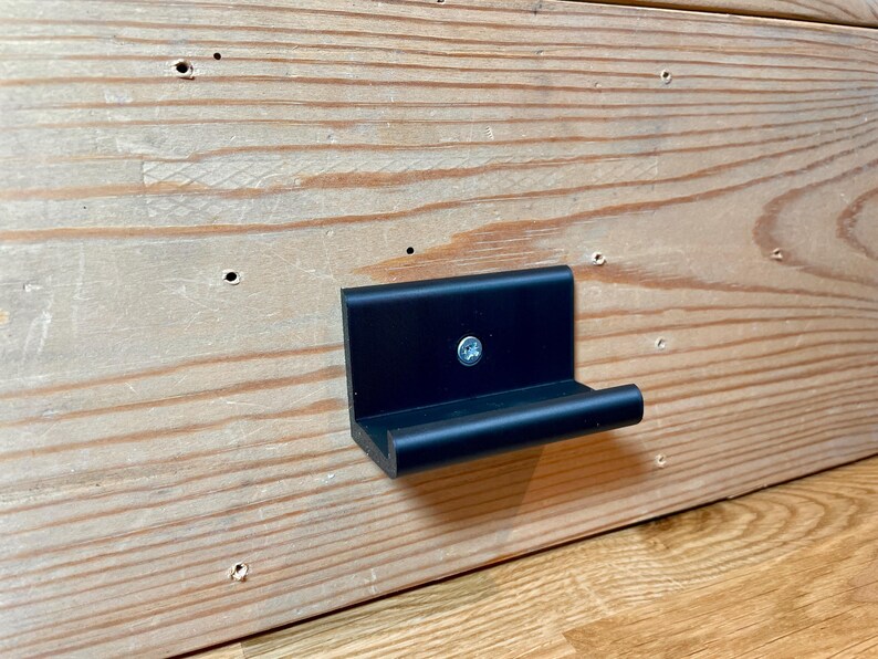 May include: A black plastic wall mount with a small shelf. The shelf is attached to the wall with a screw.