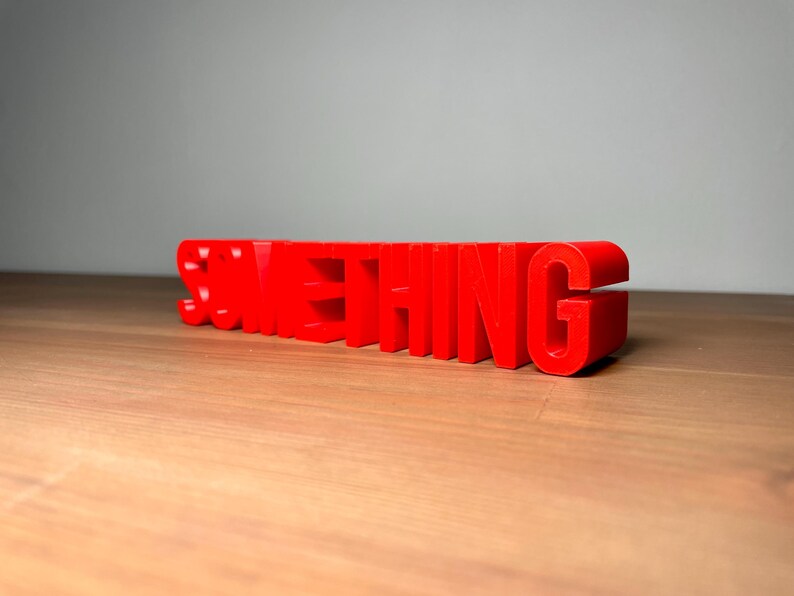 Pu&ograve; includere: Un'insegna tridimensionale rosso brillante con la scritta "SOMETHING". Le lettere sono a blocchi e si ergono su una superficie di legno. L'insegna &egrave; un pezzo d'accento vibrante.