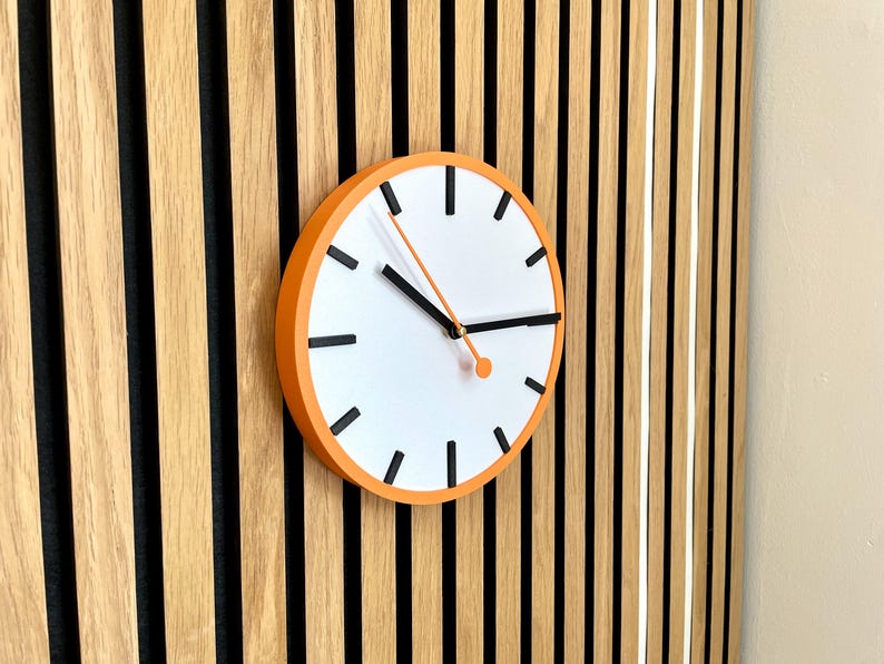 May include: A round orange clock with black hands and black markings on a white face. The clock is mounted on a wall with vertical wooden slats.