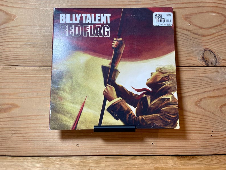 May include: A vinyl record album cover featuring a person holding a red flag with the text "BILLY TALENT RED FLAG" and the Virgin Records label with a price tag of $5.99.
