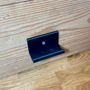 May include: A black metal bracket with a small handle attached to a wooden surface.