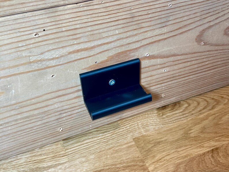 May include: A black metal bracket with a small handle attached to a wooden surface.
