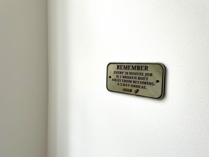 May include: A wooden sign with the text "REMEMBER EVERY 20 MINUTE JOB IS 1 BROKEN BOLT AWAY FROM BECOMING A 3 DAY ORDEAL."